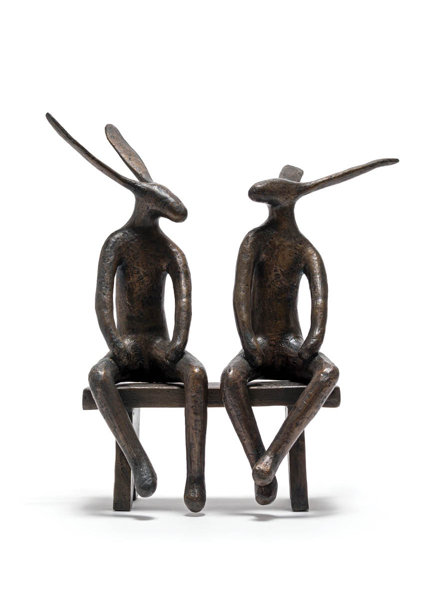 Two bronze statues of men sitting on a bench. Description generated by AI